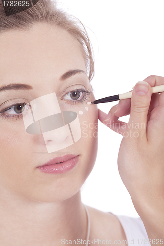 Image of young beautiful woman applying concealer on face