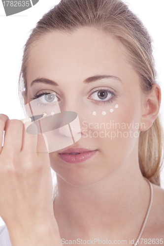 Image of young beautiful woman applying concealer on face