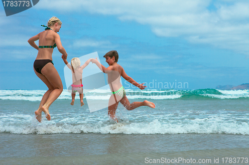 Image of Mother and two kids  jumping on beach 