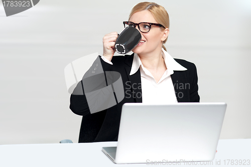 Image of Businesswoman enjoying coffee at work desk