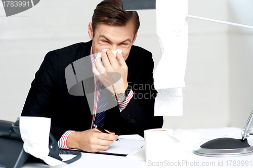 Image of Professional sitting at desk sneezing into tissue