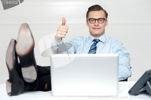 Image of Thumbs up guy relaxing with legs on work desk