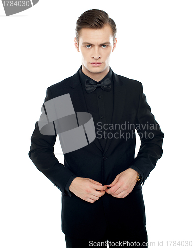 Image of Serious young man tucking coat button