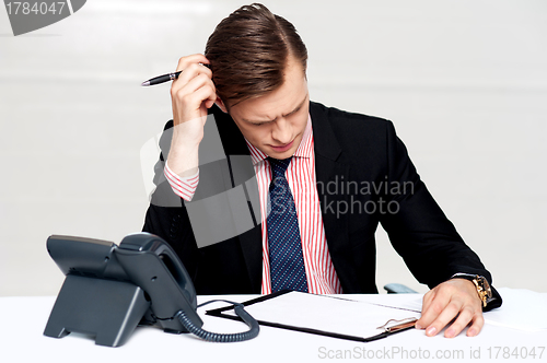 Image of Confused young man itching his head with pen