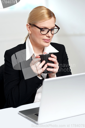 Image of Female executive looking at laptop holding mug