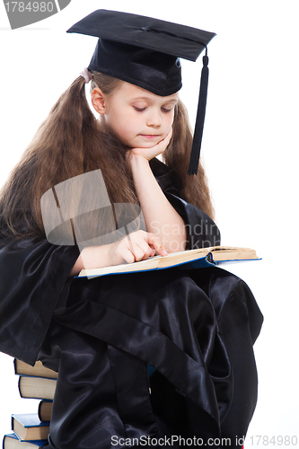 Image of girl in black academic cap and gown reading big blue book