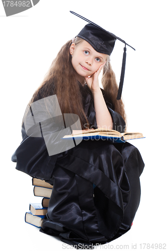 Image of girl in black academic cap and gown reading big blue book