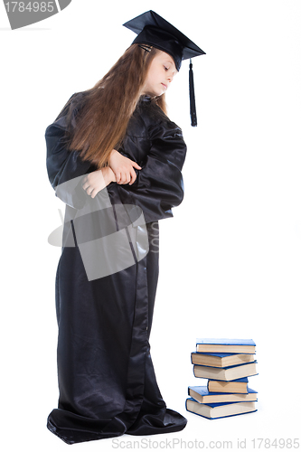 Image of girl in black academic cap and gown looking at the pile of books