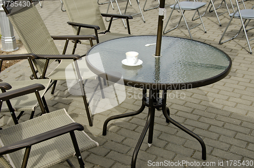 Image of Empty coffee cup on table and chairs on pavement 