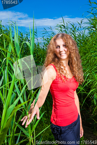 Image of beautiful girl in red among high green grass of summer meadow