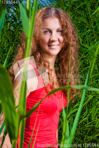 Image of beautiful girl in red among high green grass of summer meadow