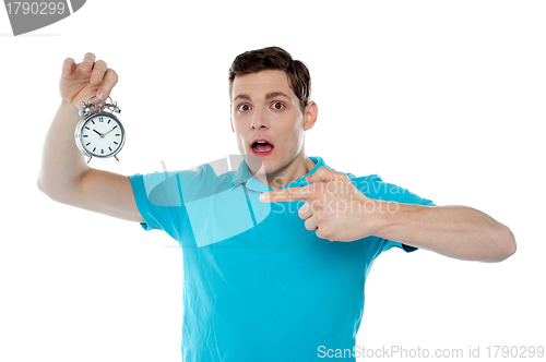 Image of Shocked young guy holding alarm clock