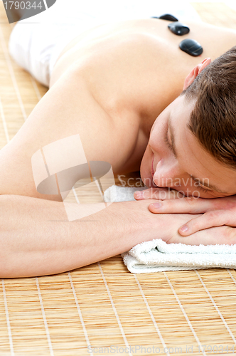 Image of Man relaxing on carpet with hot stones