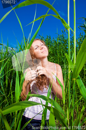 Image of beautiful girl braiding a plait among high green grass of summer meadow