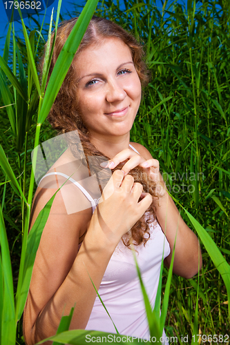 Image of beautiful girl braiding a plait among high green grass of summer meadow