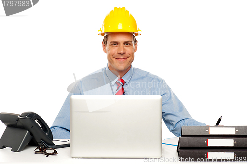 Image of Architect wearing safety hat and using laptop