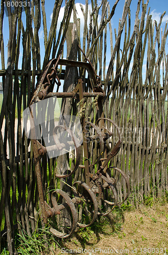 Image of Old corroded field harrow tool stand wooden fence 