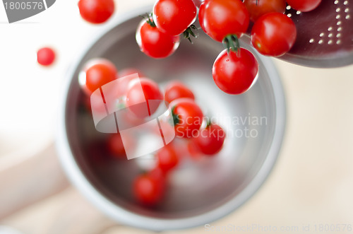 Image of Cherry Tomatoes Tumbling From Metal Colander Into Metal Pan