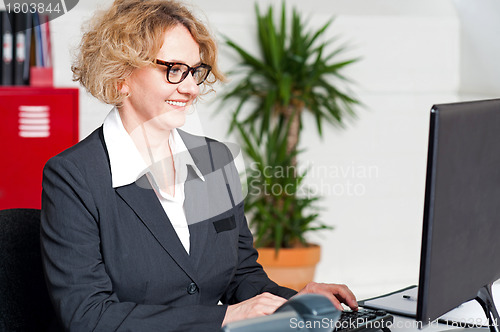 Image of Aged woman in eyeglasses working on computer