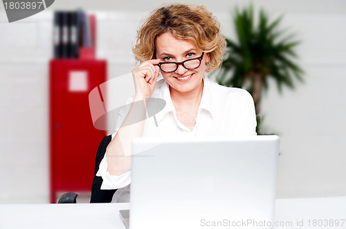 Image of Aged woman holding glasses working on laptop