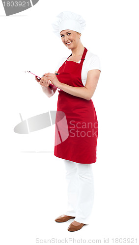 Image of Pretty female cook writing recipe on notepad