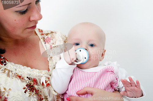 Image of baby with a pacifier in the arms of mother