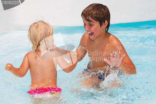 Image of Little baby girl with her brother swimming in the pool 