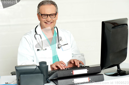 Image of Aged male doctor in glasses working on computer