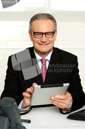 Image of Senior executive sitting with tablet pc in hands