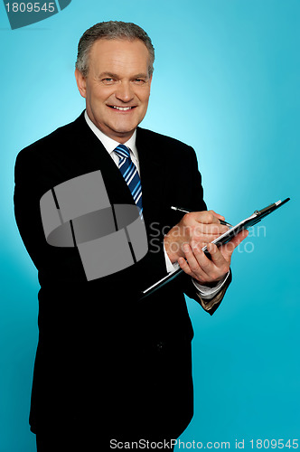 Image of Smiling businessman writing on clipboard