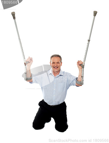 Image of Cheerful senior man holding crutches upwards