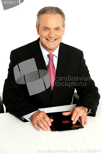 Image of Senior businessman sitting with tablet on desk