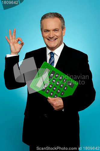 Image of Confident executive holding calculator and gesturing okay sign