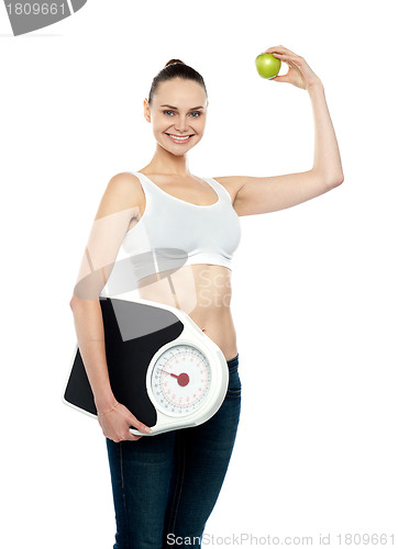 Image of Fit woman holding weighing machine and green apple