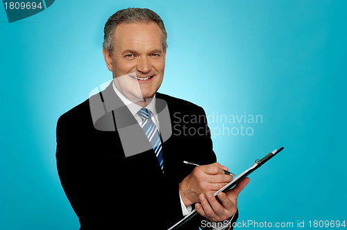 Image of Attractive senior man writing on clipboard