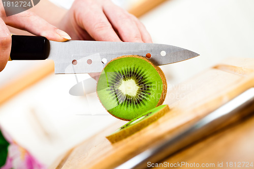 Image of Woman's hands cutting kiwi