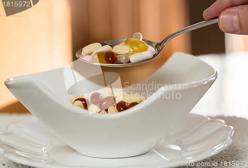 Image of Spoon of vitamins over bowl of tablets