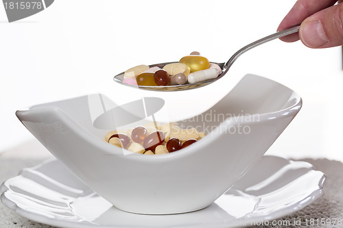 Image of Spoon of vitamins over bowl of tablets