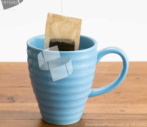 Image of Brown organic green tea bag lowered in mug