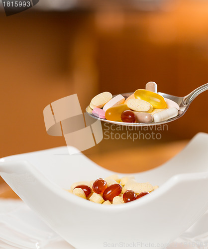 Image of Spoon of vitamins over bowl of tablets