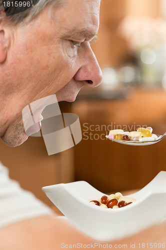 Image of Senior man eating a spoon of vitamins