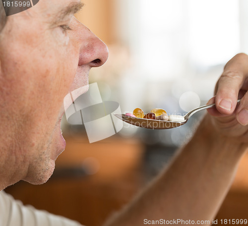 Image of Senior man eating a spoon of vitamins