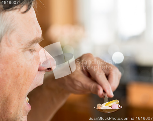 Image of Senior man eating a spoon of vitamins