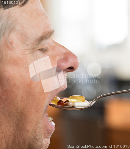 Image of Senior man eating a spoon of vitamins