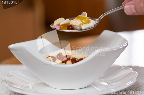 Image of Spoon of vitamins over bowl of tablets