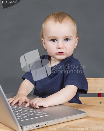 Image of baby with laptop computer in grey background