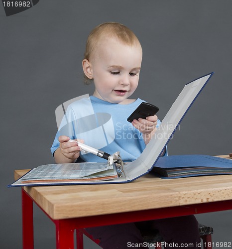 Image of baby with paperwork and calculator at wooden desk