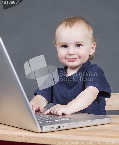 Image of baby with laptop computer in grey background