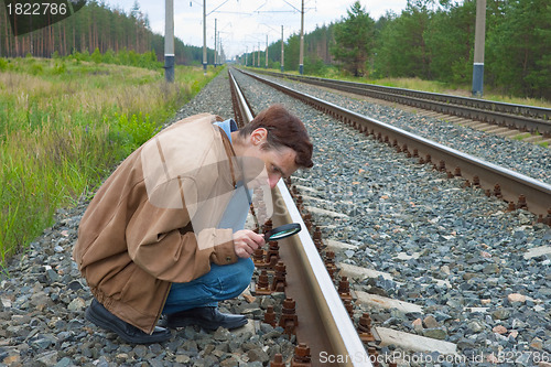 Image of Man sits on railway with magnifier in hand