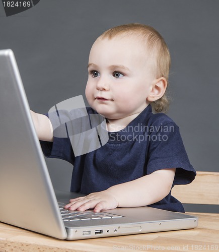 Image of baby with laptop computer in grey background